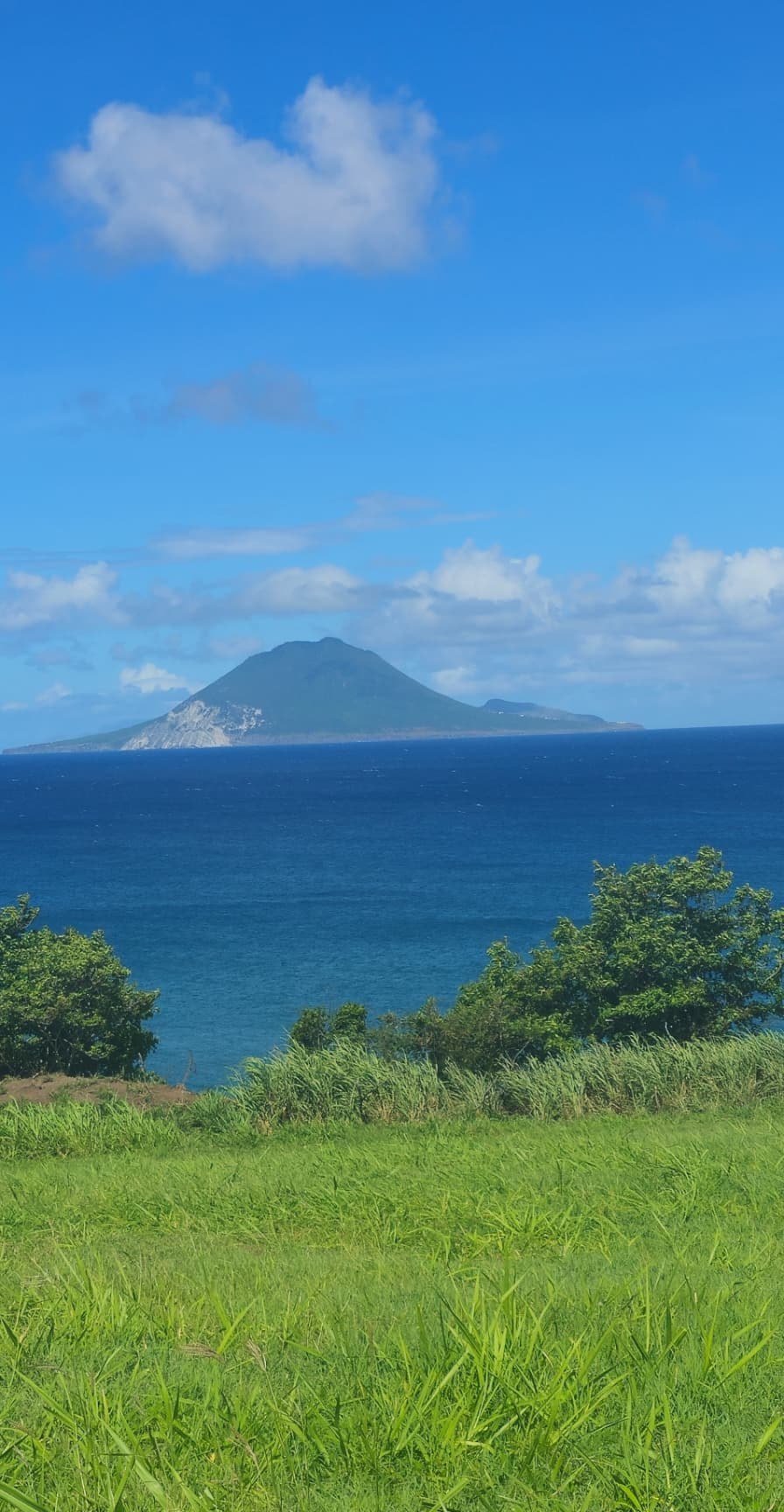 Grassy hillside overlooking the sea with a volcanic island peak on the horizon